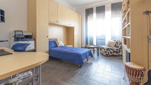 Ein Schlafzimmer mit einem Bett, Schreibtisch, Drucker und einem kleinen Tisch mit Schachbrett.