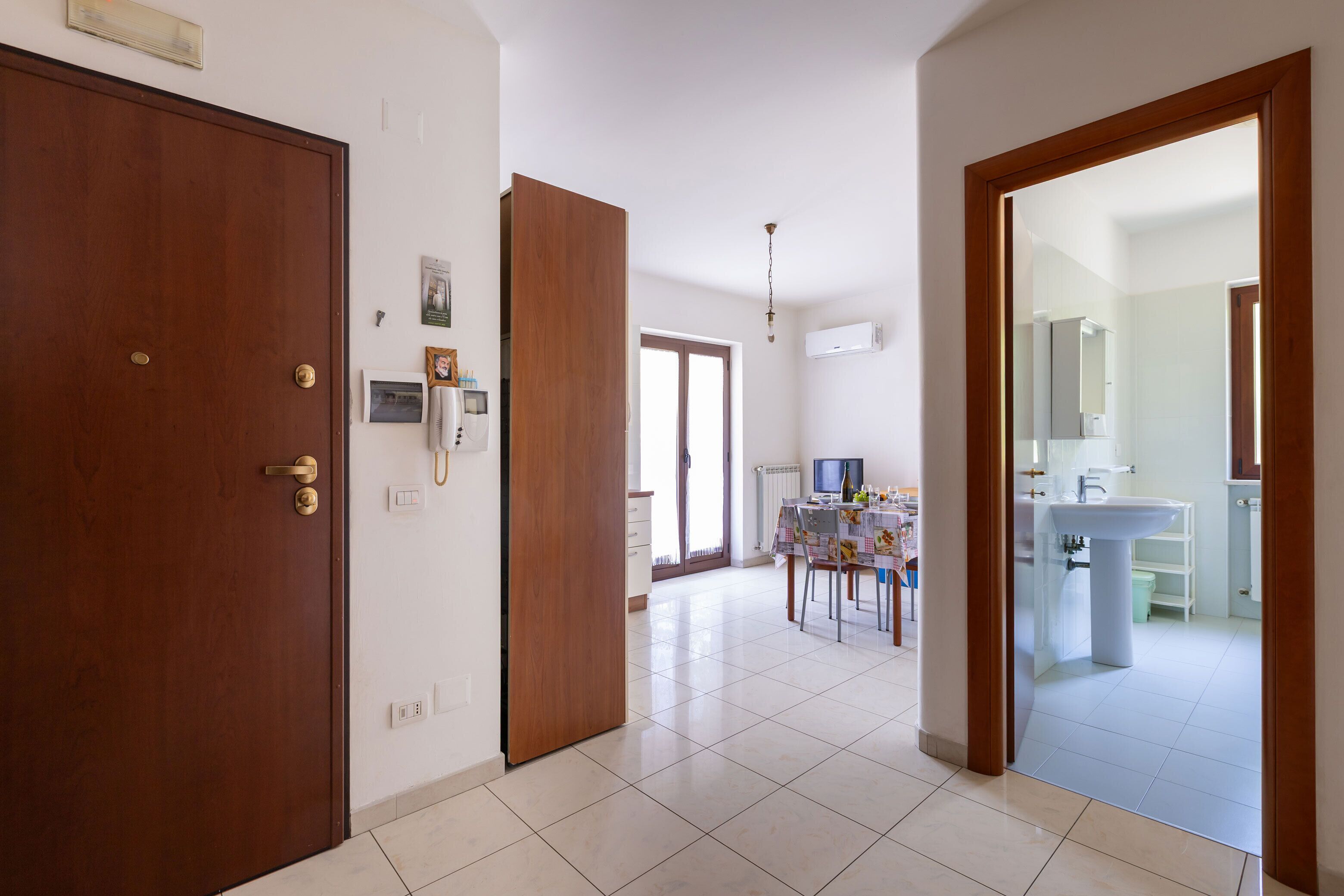 A spacious hallway with a wooden door, a dining area with a table and chairs, and a bathroom with a sink and mirror.
