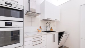 Una cocina moderna con armarios blancos, horno empotrado, lavavajillas y pileta de acero inoxidable.