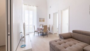 Una sala de estar moderna con un sofá beige, un comedor con mesa y sillas, y una cocina con mostrador y electrodomésticos.