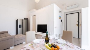 Una sala de estar moderna con un sofá, una mesa de comedor con fruteros y copas de vino, un televisor de pantalla plana y una puerta blanca.