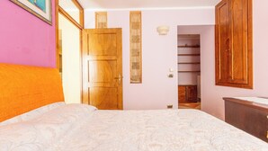 Quarto com cama, guarda-roupa de madeira e roupeiro embutido com prateleiras.
