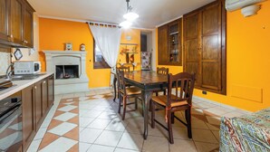 Uma sala de jantar com mesa e cadeiras de madeira, lareira branca e cozinha com armários de madeira e micro-ondas.