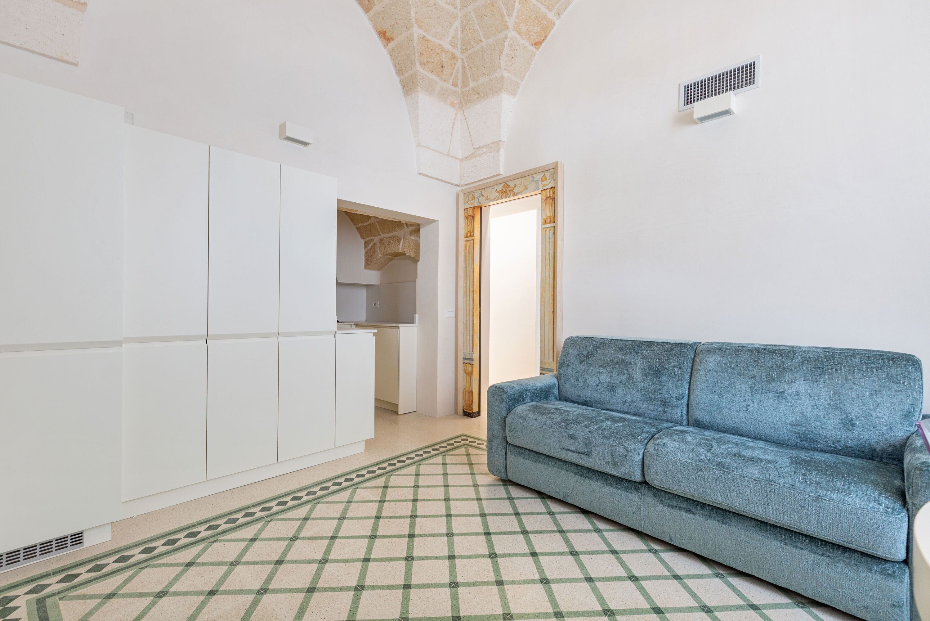 Une pièce avec un canapé bleu, des meubles blancs, un tapis à motifs et un plafond décoratif.