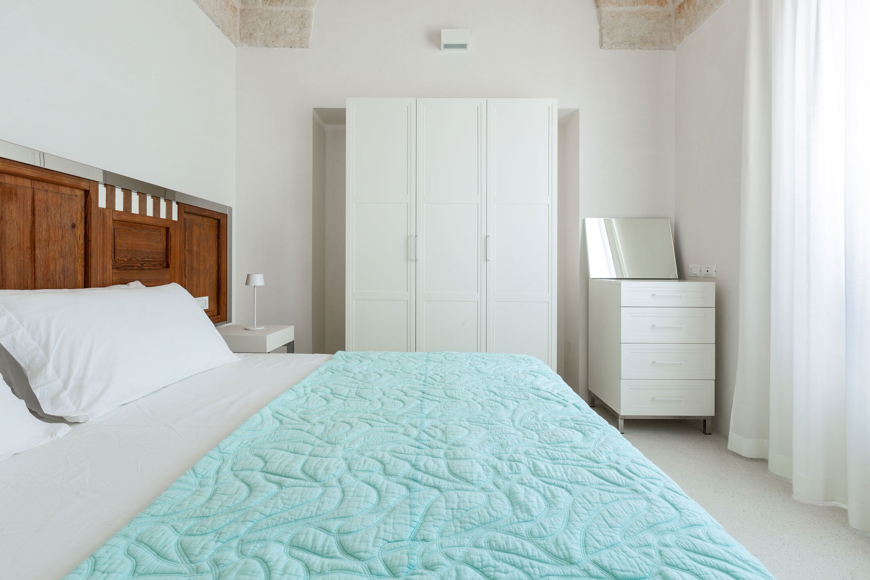 Un dormitorio con cama, armario, mesita de noche y espejo.