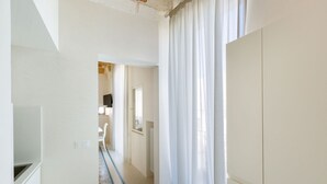 Un couloir aux murs blancs, avec un radiateur et une porte donnant sur une autre pièce.