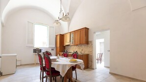 Comedor con una mesa dispuesta para cuatro, armarios de madera y una cocina al fondo.
