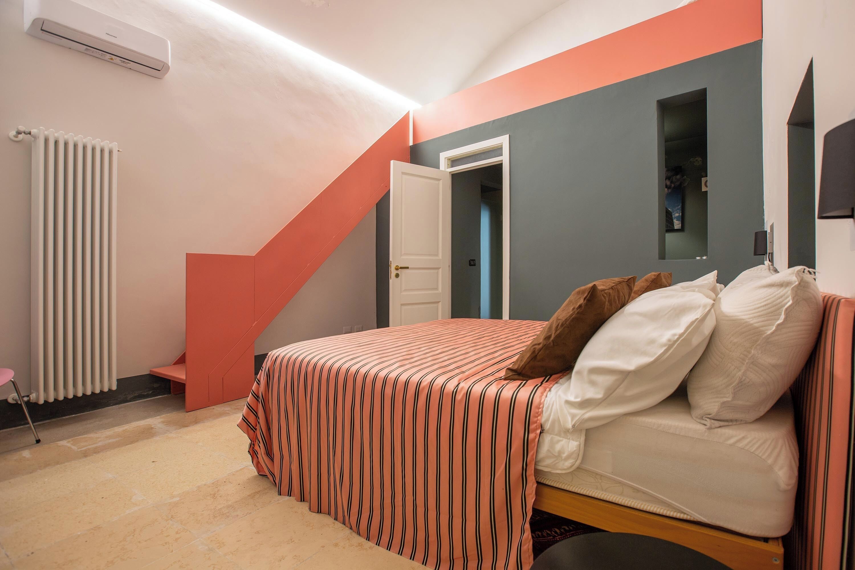 Quarto com cama, radiador, porta e uma pequena mesa.