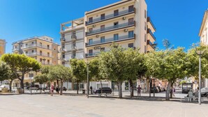 Un immeuble à plusieurs étages, doté de balcons, se dressant sous un ciel d’un bleu limpide.