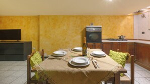 Un coin repas avec une table dressée pour quatre personnes, un téléviseur et une cuisine en arrière-plan.
