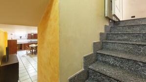 Un escalier menant à un deuxième étage, avec un coin cuisine visible au fond.