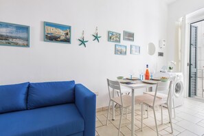 A modern living room with a blue sofa, a dining table with chairs, and a washing machine. - Il Balconcino del Borgo by BarbarHouse (Monopoli)