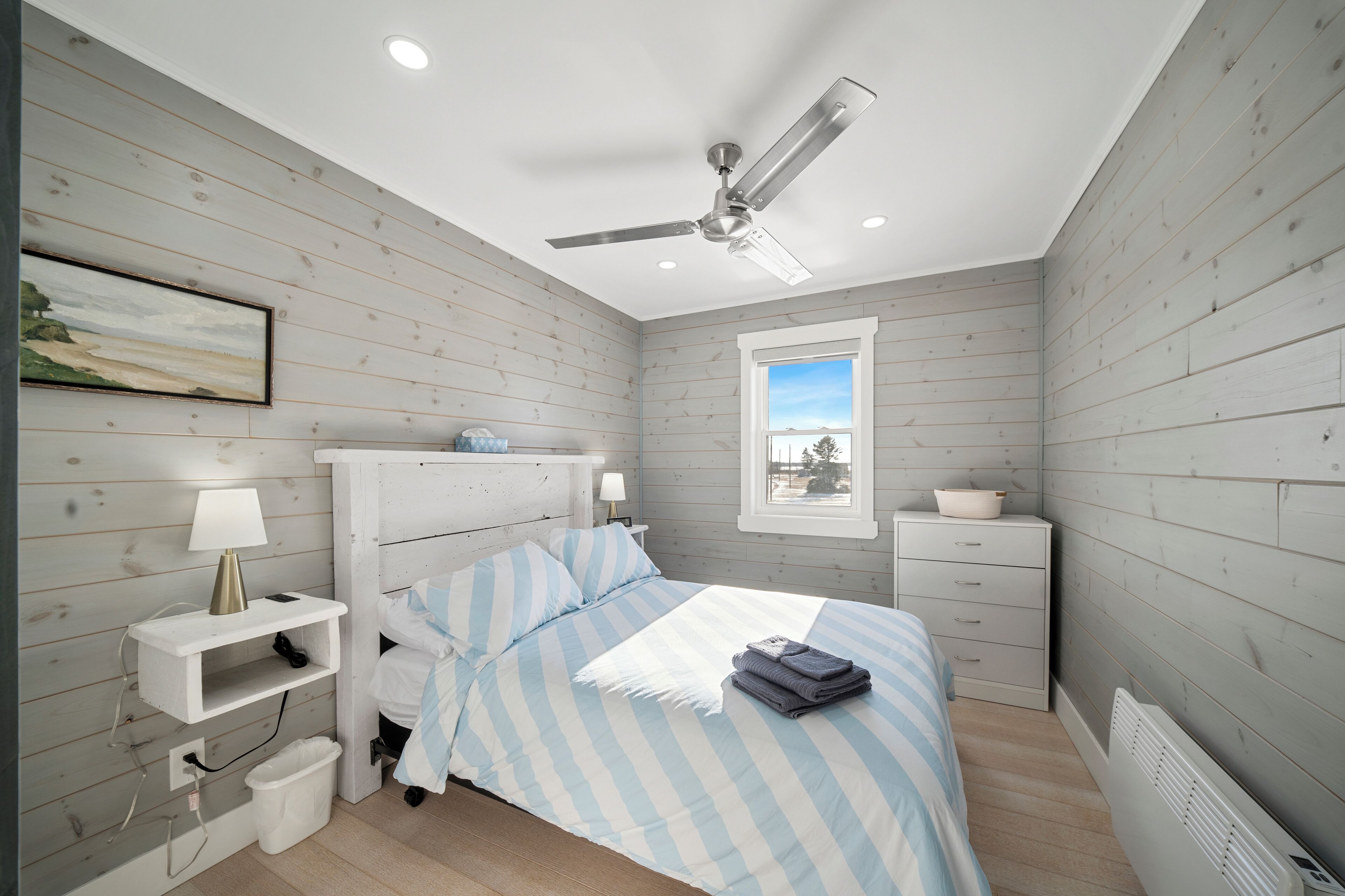 A bedroom with a bed, nightstands, a ceiling fan, a window, and a radiator.