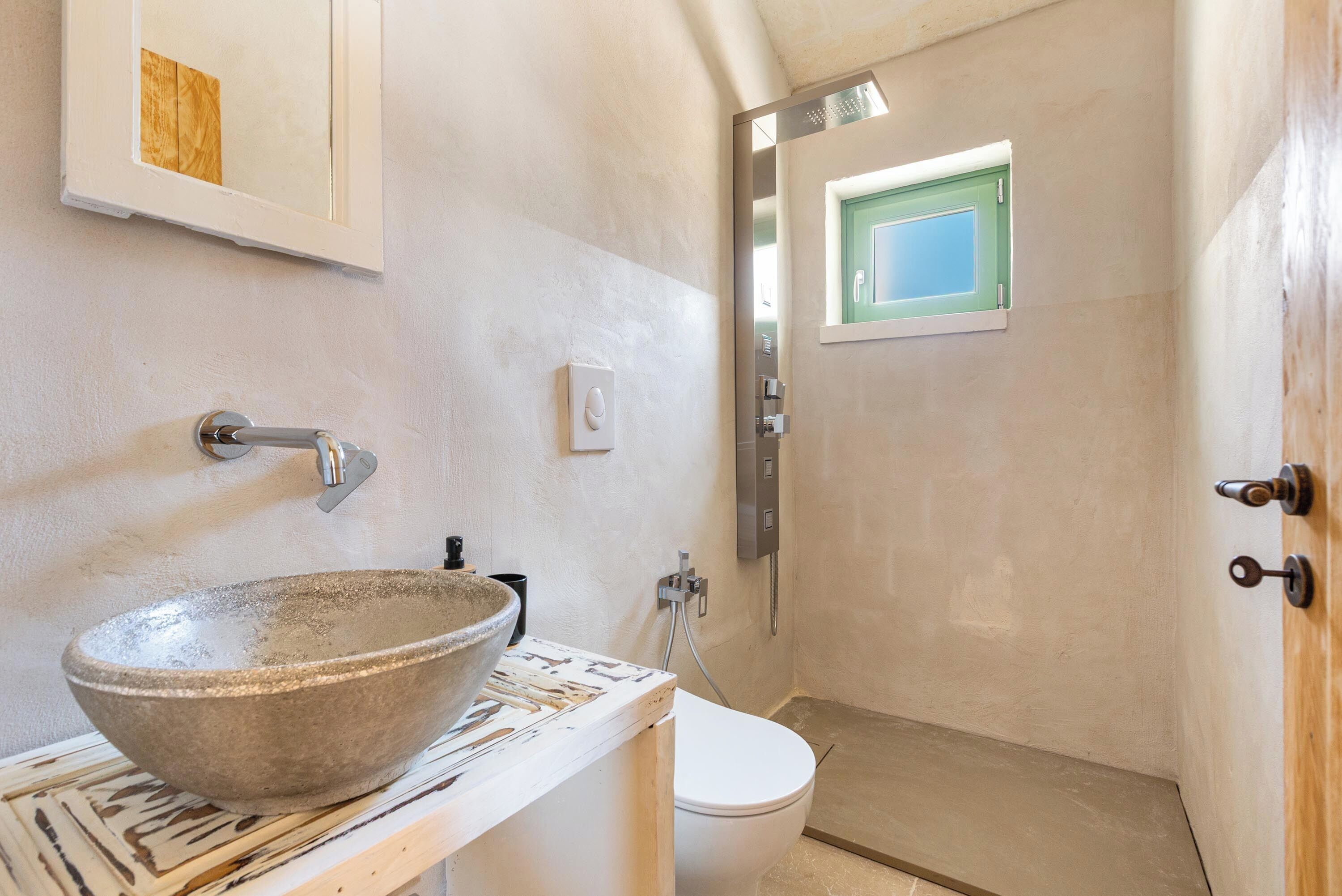 A bathroom with a large stone basin, a toilet, and a shower area.