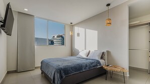 A modern bedroom with a large bed, a TV mounted on the wall, a small round table, and a view of a building through the window. - Apartment 5 min from beautiful beach for 6 guests  (Cartagena de Indias)