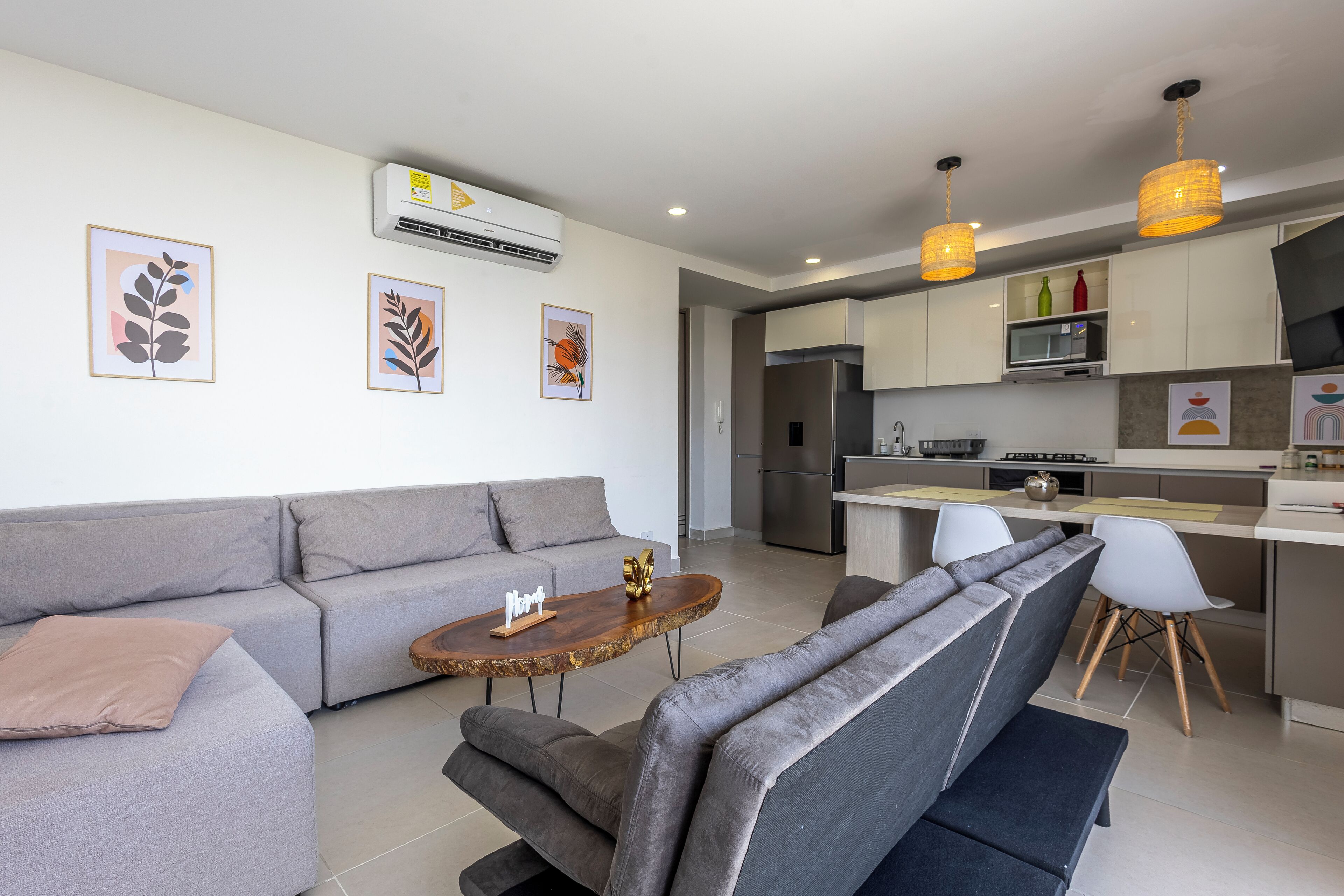 Un salon moderne avec un canapé gris, une table basse en bois et un coin repas avec des chaises blanches.