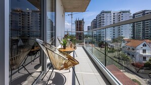Un balcon avec des fauteuils en osier et une petite table, d’où l’on peut admirer un paysage urbain composé d’immeubles modernes et d’une grue de construction.