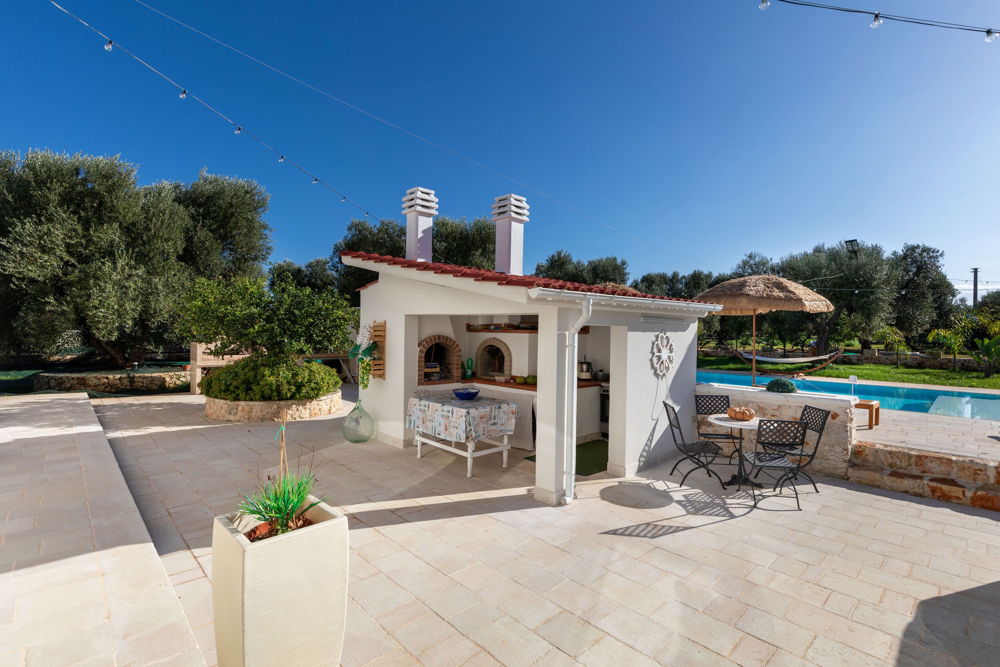 Un'area patio con una piccola struttura bianca, mobili da esterno e una piscina.