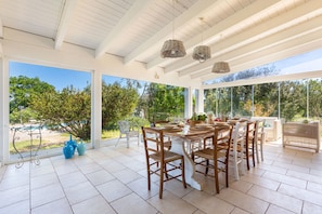 Eine überdachte Terrasse mit Esstisch, Stühlen und hängenden Korblampen.