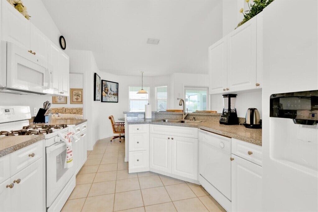 Una cocina moderna con muebles blancos, una estufa integrada y una isla grande con un fregadero.