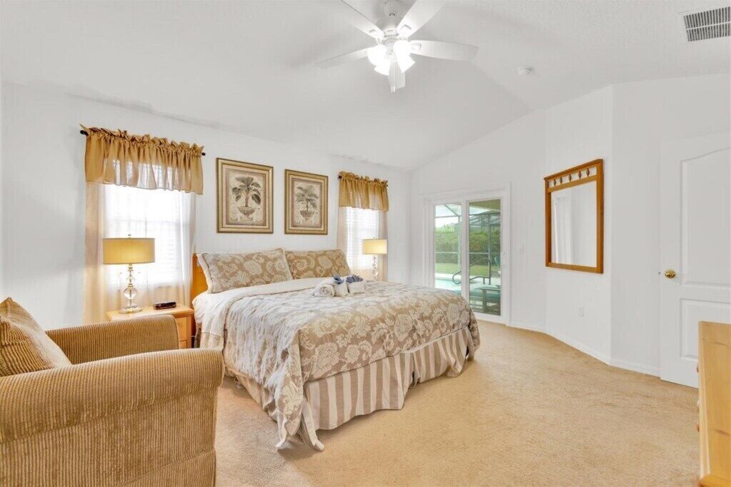 A bedroom with a large bed, two bedside tables with lamps, a chair, and a ceiling fan.