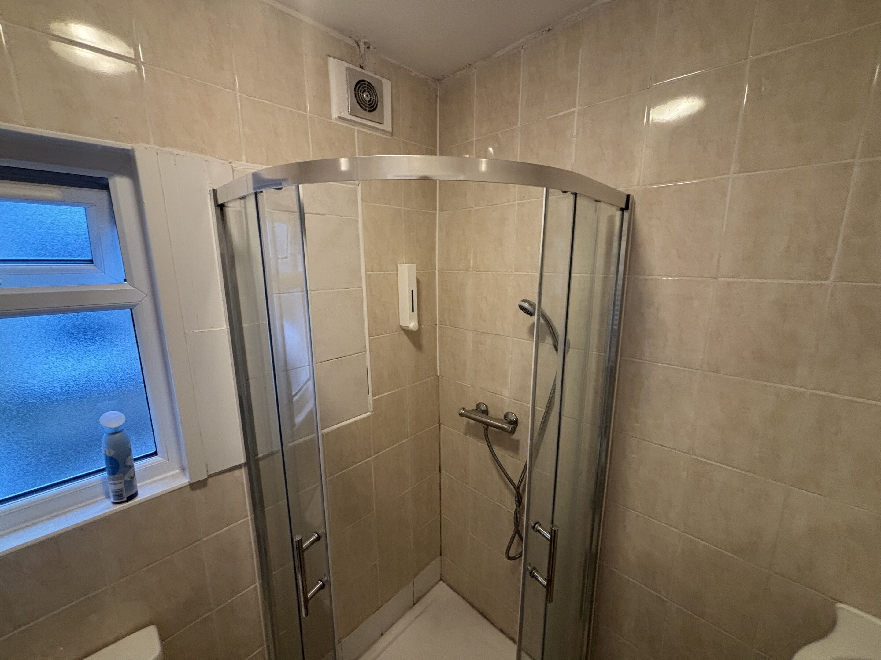 A glass-enclosed shower with a handheld showerhead, a handheld showerhead, and a handheld showerhead.