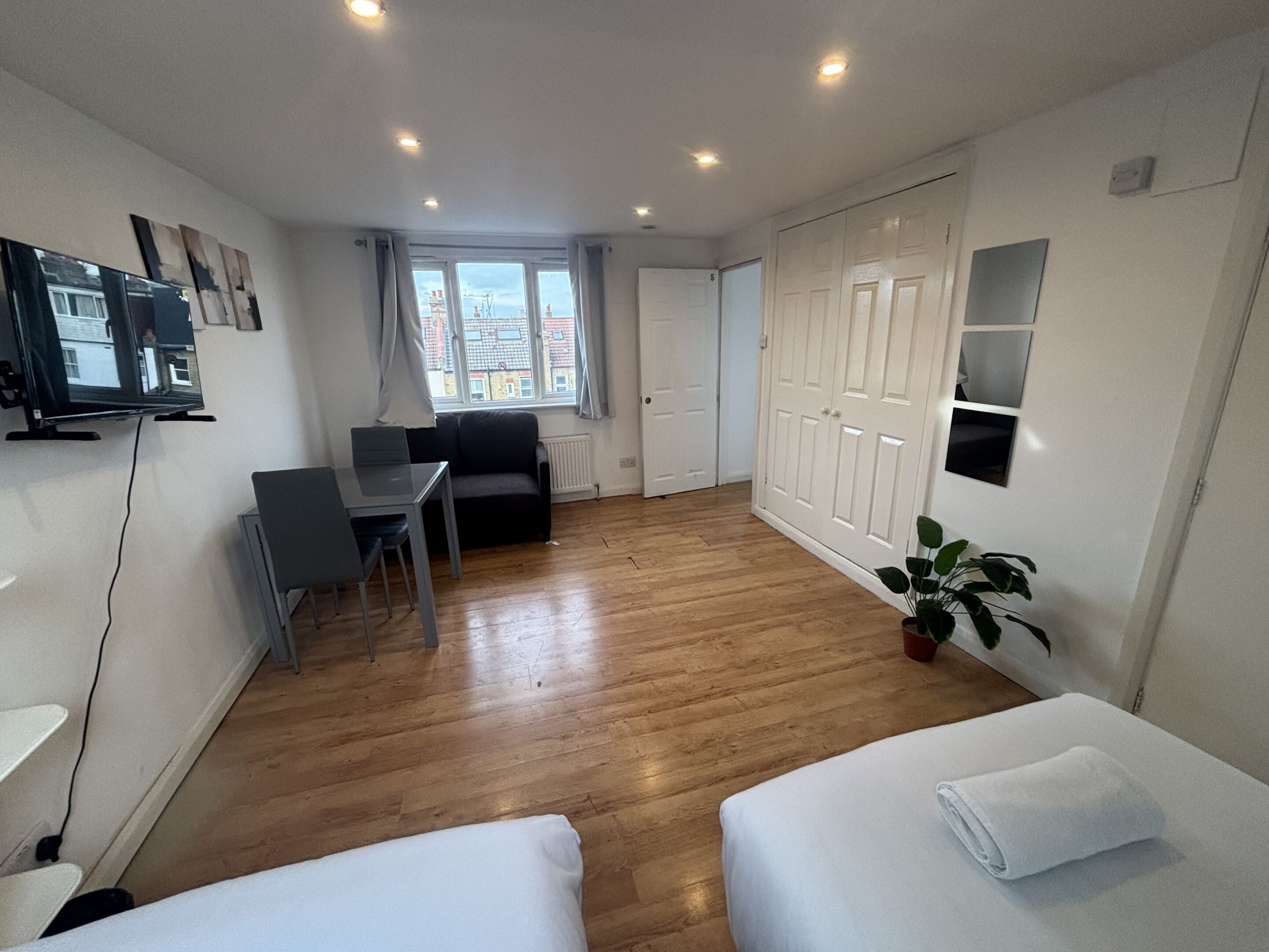 Ein modernes Hotelzimmer mit Holzboden, einer Couch, einem Schreibtisch, einem Fernseher und einem Kleiderschrank.