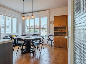A modern kitchen with wooden cabinets, a dining area with a round table and chairs, and large windows offering a view of the neighborhood. - Ca dei Noni by Interhome (Riva del Garda)