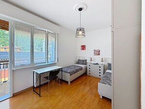 A modern bedroom with a desk, two beds, a radiator, and a window with blinds. - Ca dei Noni by Interhome (Riva del Garda)