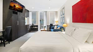 A modern hotel room with a large bed, a desk, a chair, a TV mounted on the wall, and a red accent wall. - Stylish Central Studio With Gym (Melbourne)