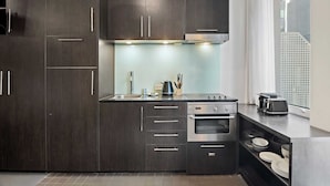A modern kitchen with dark wood cabinets, stainless steel appliances, and a window providing a view of the city. - Stylish Central Studio With Gym (Melbourne)