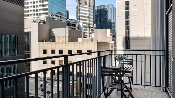 A balcony with a table and chair, overlooking a cityscape with modern buildings. - Stylish Central Studio With Gym (Melbourne)