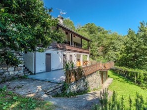 Une maison à deux étages, avec des fondations en pierre, un balcon et une clôture en bois.