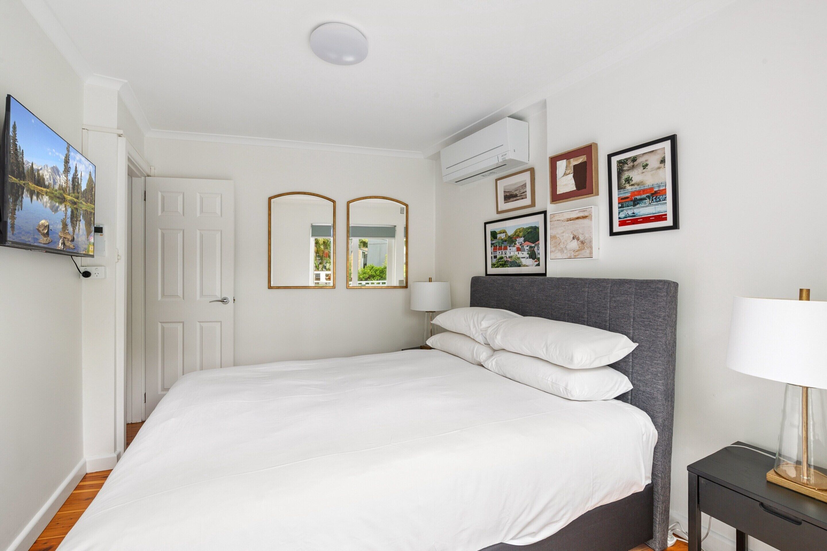 Un dormitorio ordenado con cama, mesita de noche y aire acondicionado de pared.