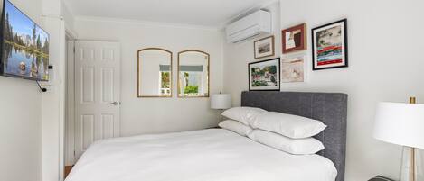 Un dormitorio ordenado con cama, mesita de noche y aire acondicionado de pared.