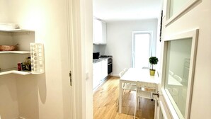 Cozinha moderna com armários brancos, área de jantar com mesa e cadeiras brancas, e piso de madeira.
