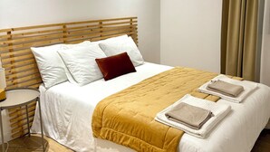 Cama bem arrumada com roupa de cama branca e castanha, cabeceira de madeira e mesa de cabeceira com abajur.