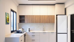 Cocina moderna con armarios blancos, un panel de madera decorativo, horno empotrado y refrigerador.