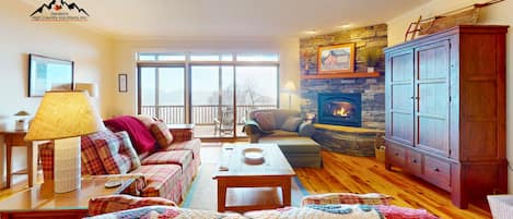 Una sala de estar acogedora con chimenea, un sofá, una mesa de centro y vistas amplias por las ventanas.