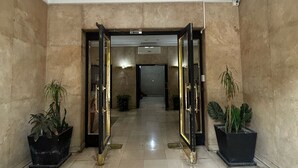 Een ruime lobby met een hoge plafond, grote kamerplanten en een betegelde vloer.