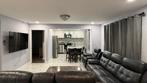 A modern living room with a leather sofa, a flat-screen TV, and a dining area with a kitchen in the background. - Delightful 3-bedroom house in charming Tucker (Tucker)