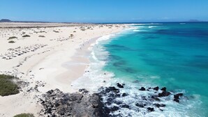 Ein Strand mit klarem türkisblauem Wasser, sandigem Ufer und Felsformationen.