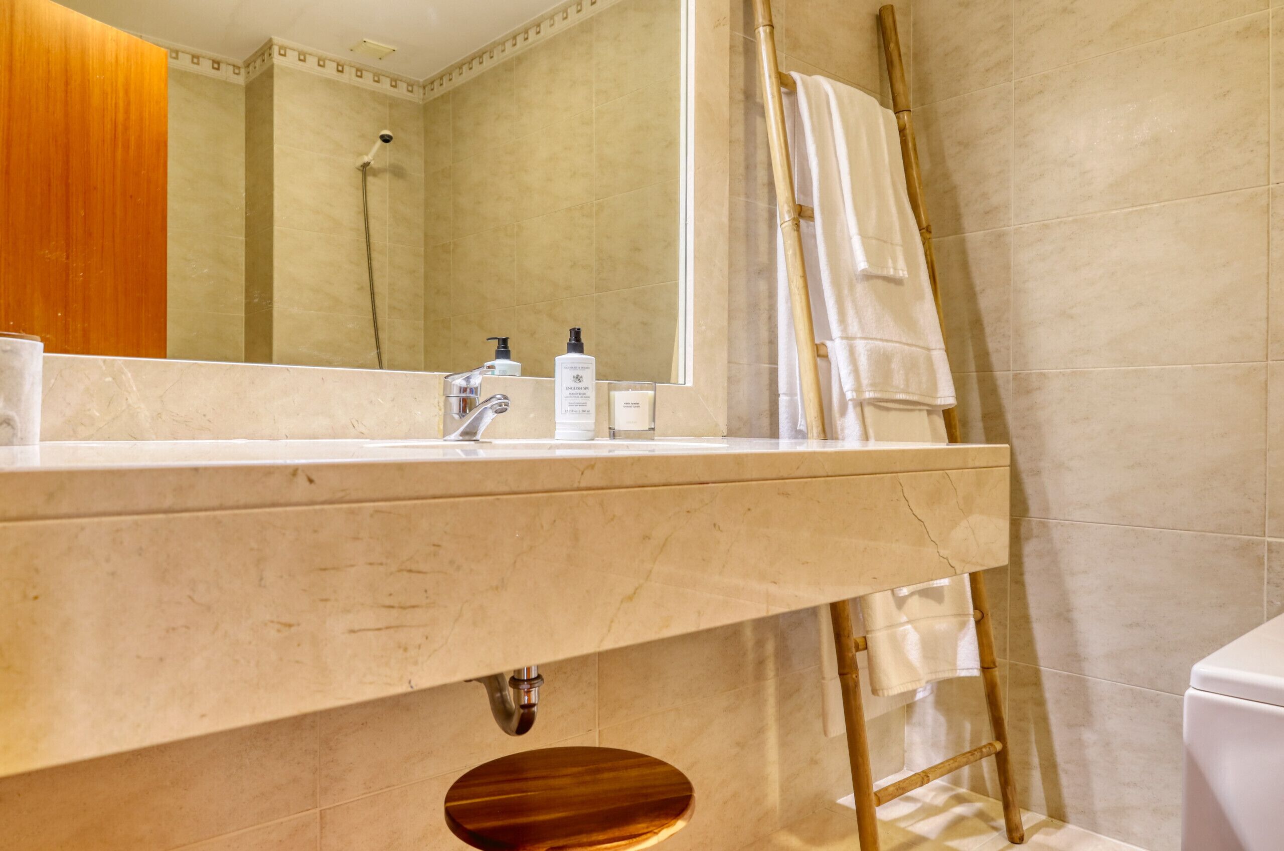 Un baño con lavamanos de mármol, un espejo, ducha e inodoro.