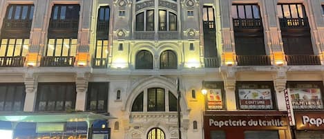 A historic building with ornate architecture, featuring a prominent clock and multiple storefronts including a bakery and a fashion store.