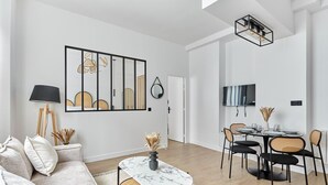 Ein modernes Wohnzimmer mit Sofa, Couchtisch und Essbereich mit Stühlen sowie einem Fernseher.