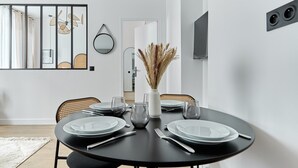 Ein moderner Essbereich mit einem runden schwarzen Tisch, gedeckt für vier Personen, umgeben von Korbstühlen.