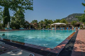 A swimming pool with lounge chairs and umbrellas, surrounded by trees and a mountain in the background. - Pineas (Kalabaka)