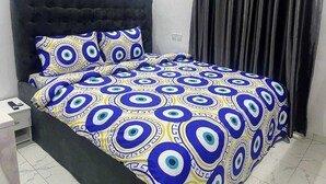 A bed with a patterned bedspread, a dark headboard, and a bedside table with a lamp. - Welcoming 1-bedroom apartment with AC in vibrant (Ikeja)