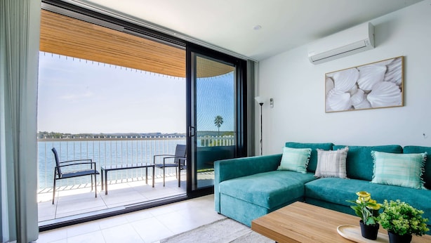 A modern living room with a teal sofa, a wooden coffee table, and a view of the sea through a sliding glass door. - Stunning 1-bed Bayside Apartment With Superb Views (Batemans Bay)