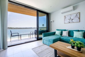 Un salon moderne avec un canapé de couleur turquoise, une table basse en bois et une vue sur la mer, visible à travers une porte-fenêtre coulissante.
